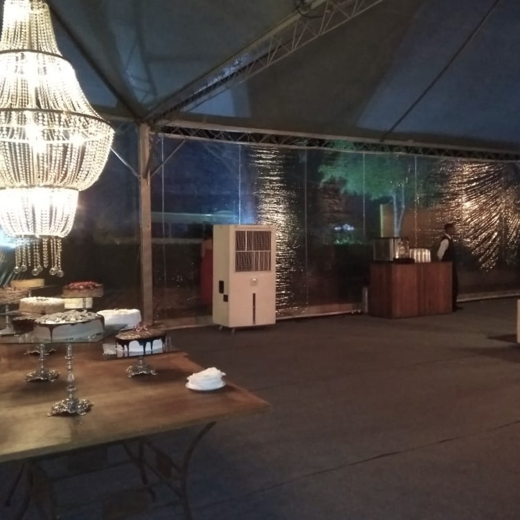 Evento noturno em tenda, com lustre e mesa de doces, climatizador portátil ao lado
