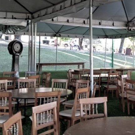 Tenda em área externa sobre gramado, com mesas de madeira e climatizador de coluna